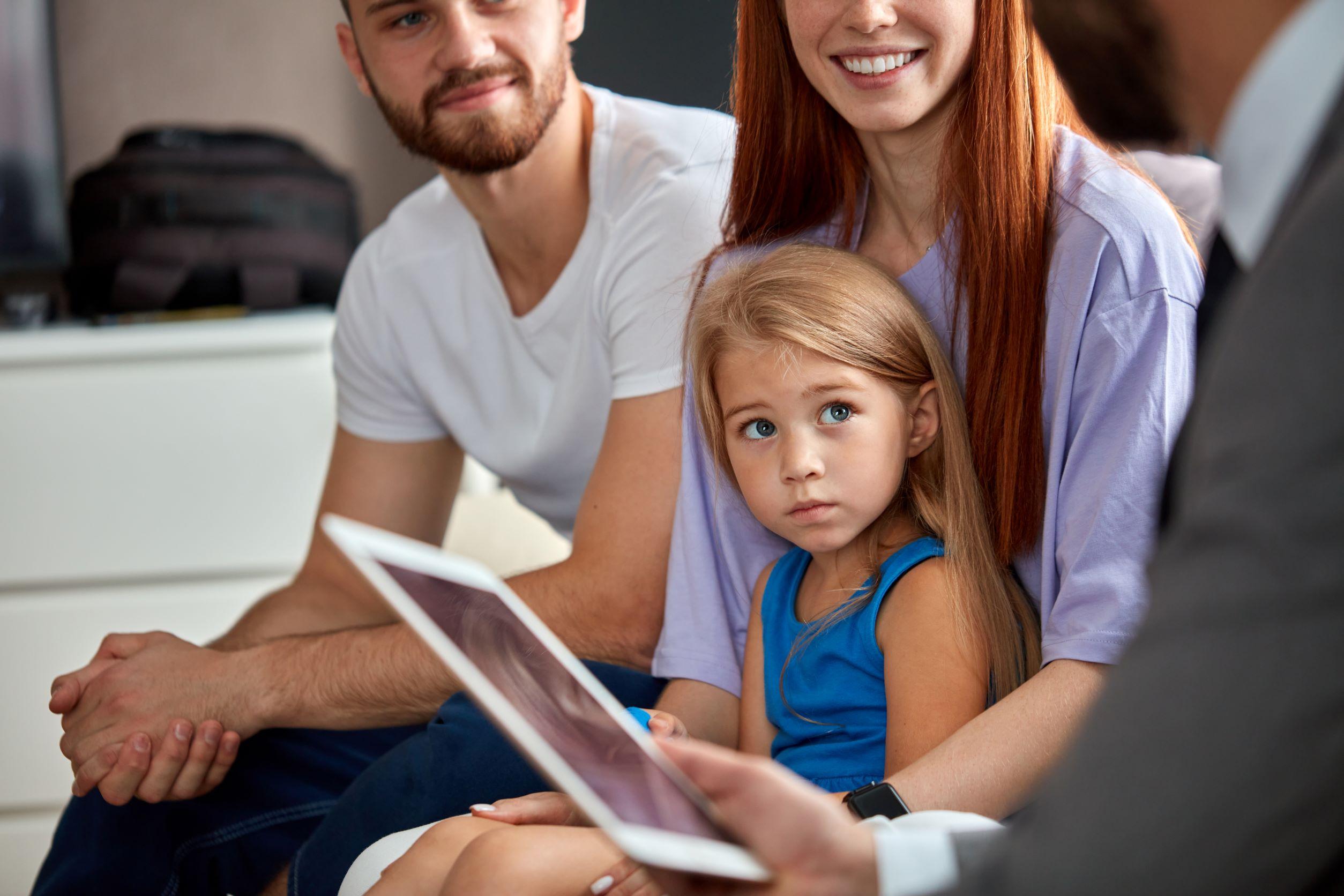 two adults holding young child talking to therapist holding ipad